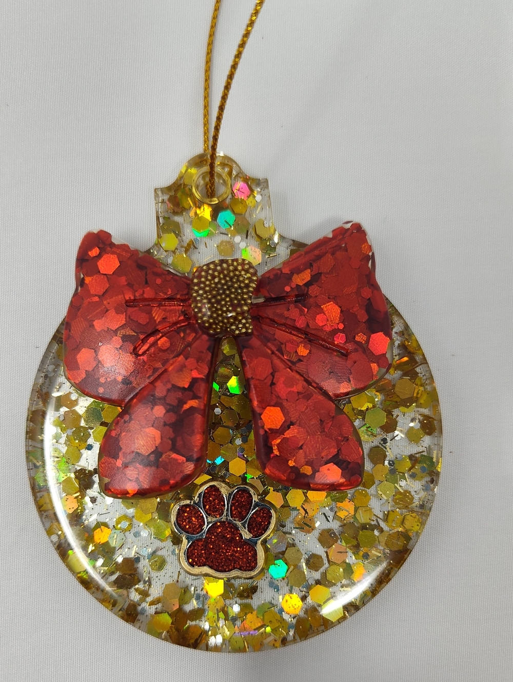 Festive Gold Holiday Ornament With Red Bow And Red Paw Print Embellishment